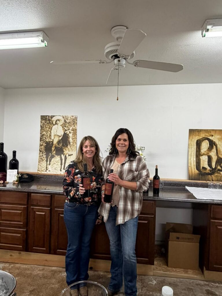 two women smiling holding wine bottles